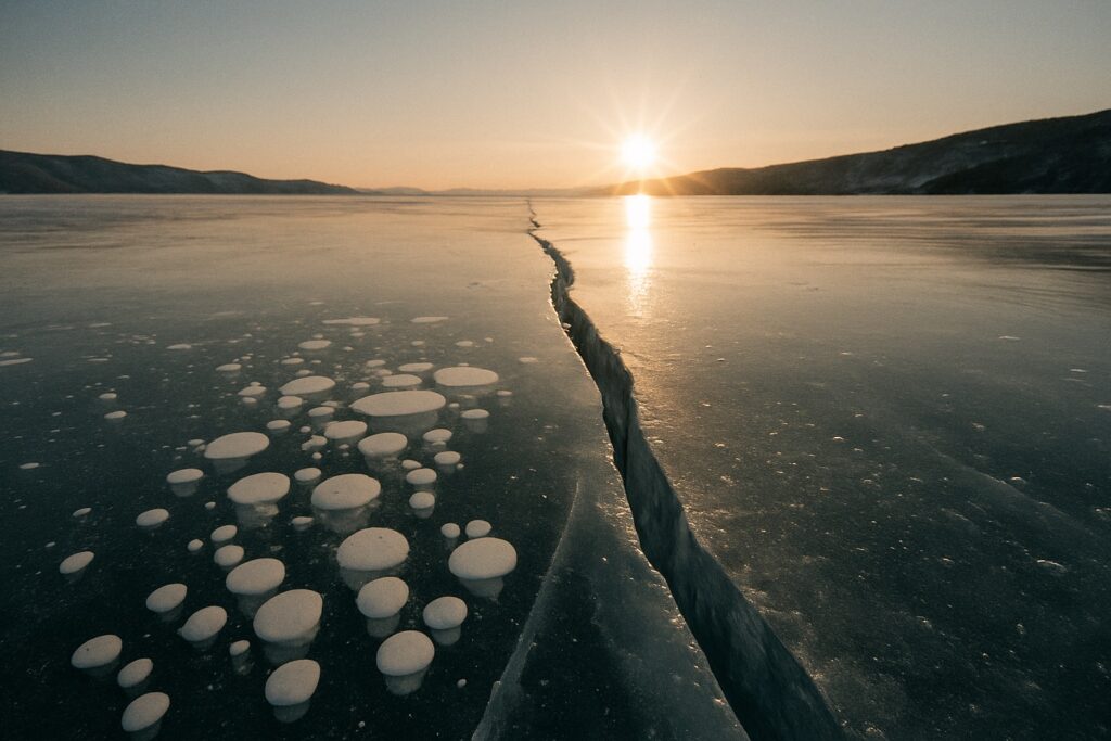 Klareis aus Bodennähe fotografiert mit Blasen und einem Riss im Vordergrund, die Sonne am Horizont