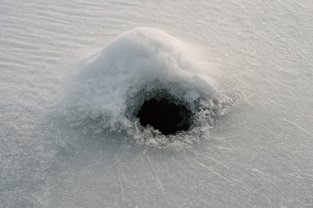 Kleines, unregelmäßiges Loch unter einer Schneekuppe auf dem Eis